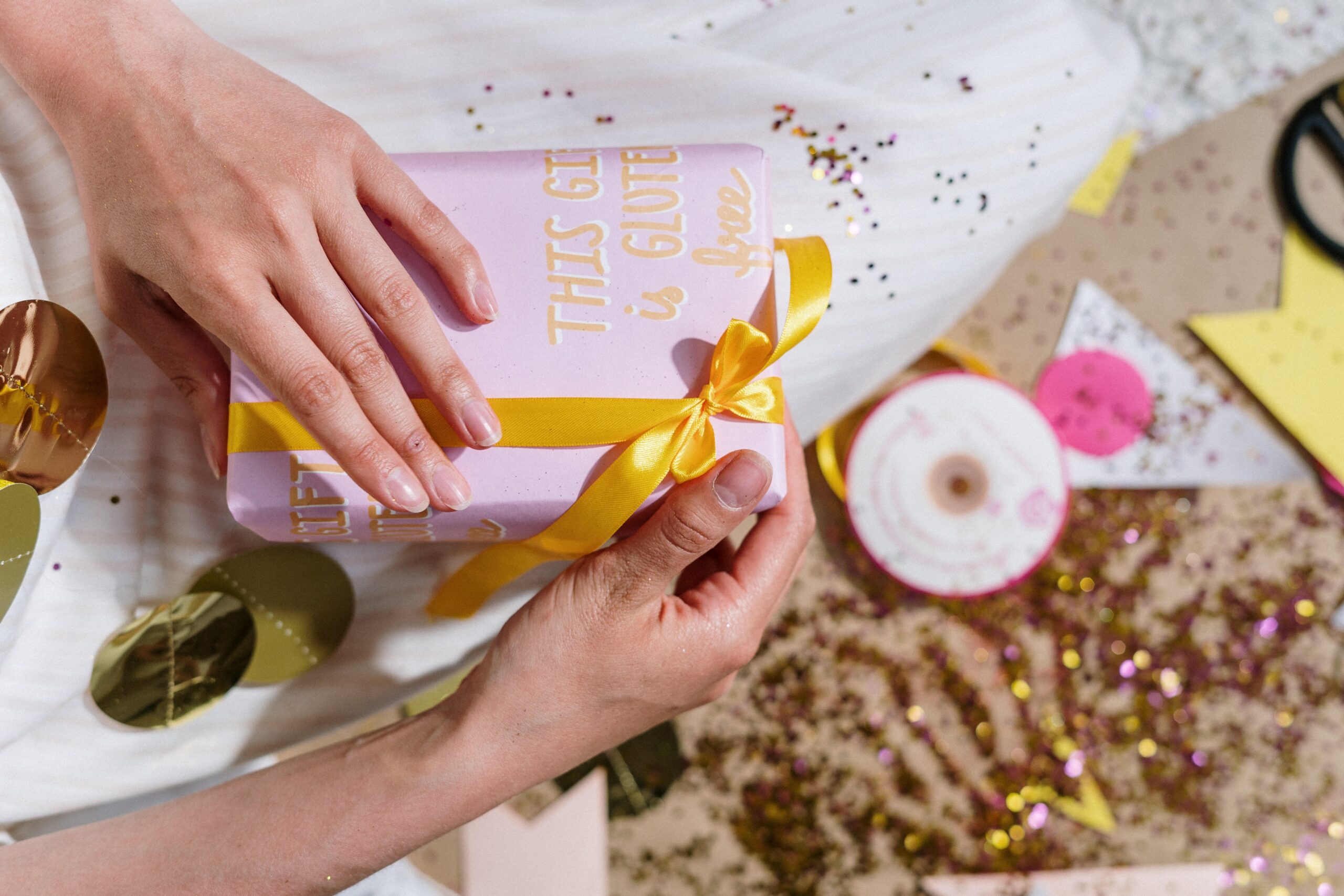 Two hands holding pink gift box with gold ribbon